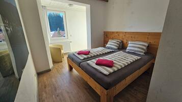 A bedroom with a wooden bed, two pillows, a red towel, and a window with a view of a building.