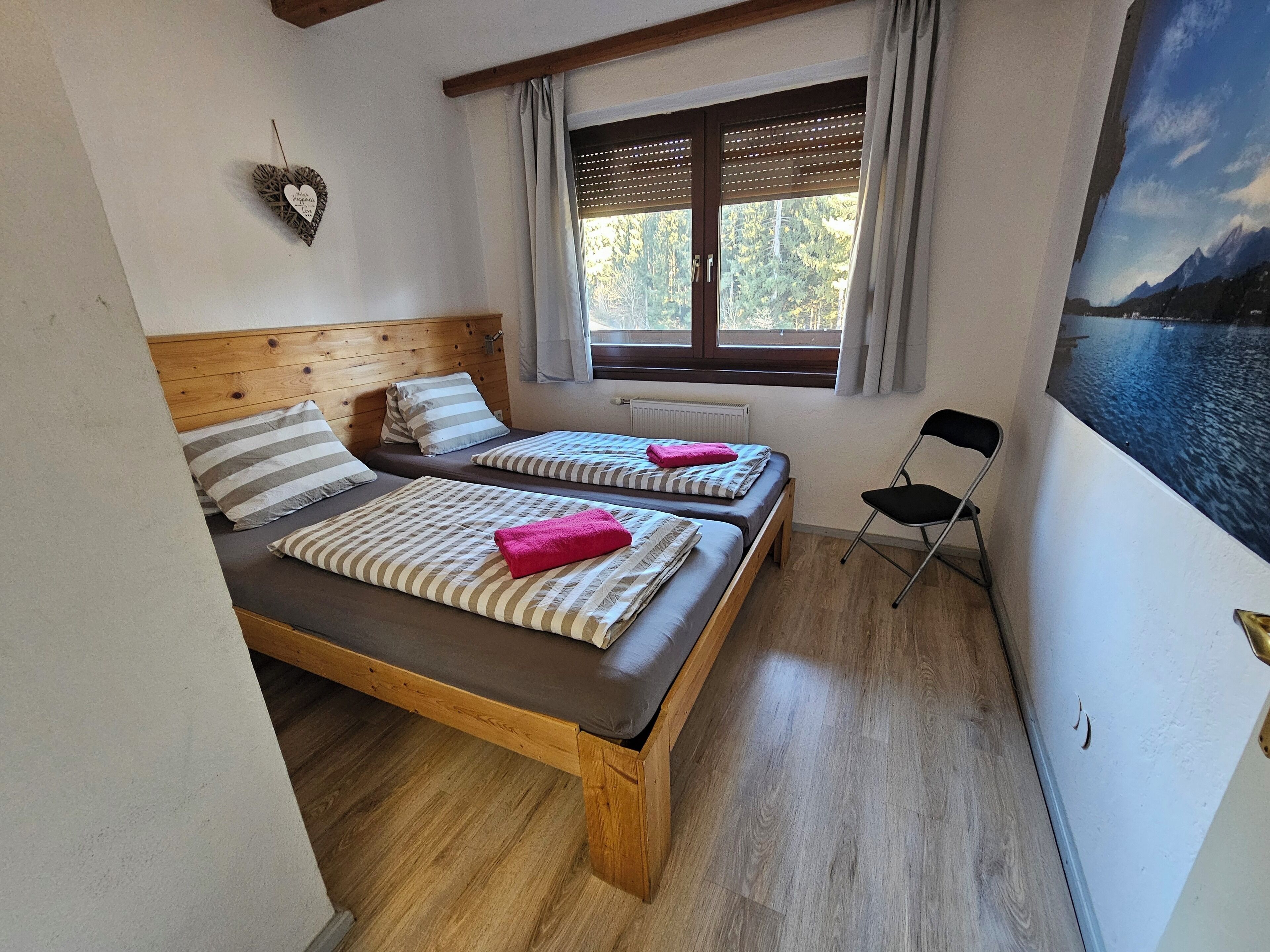 Una habitación con dos camas de madera, una ventana con persianas, un radiador y una silla.