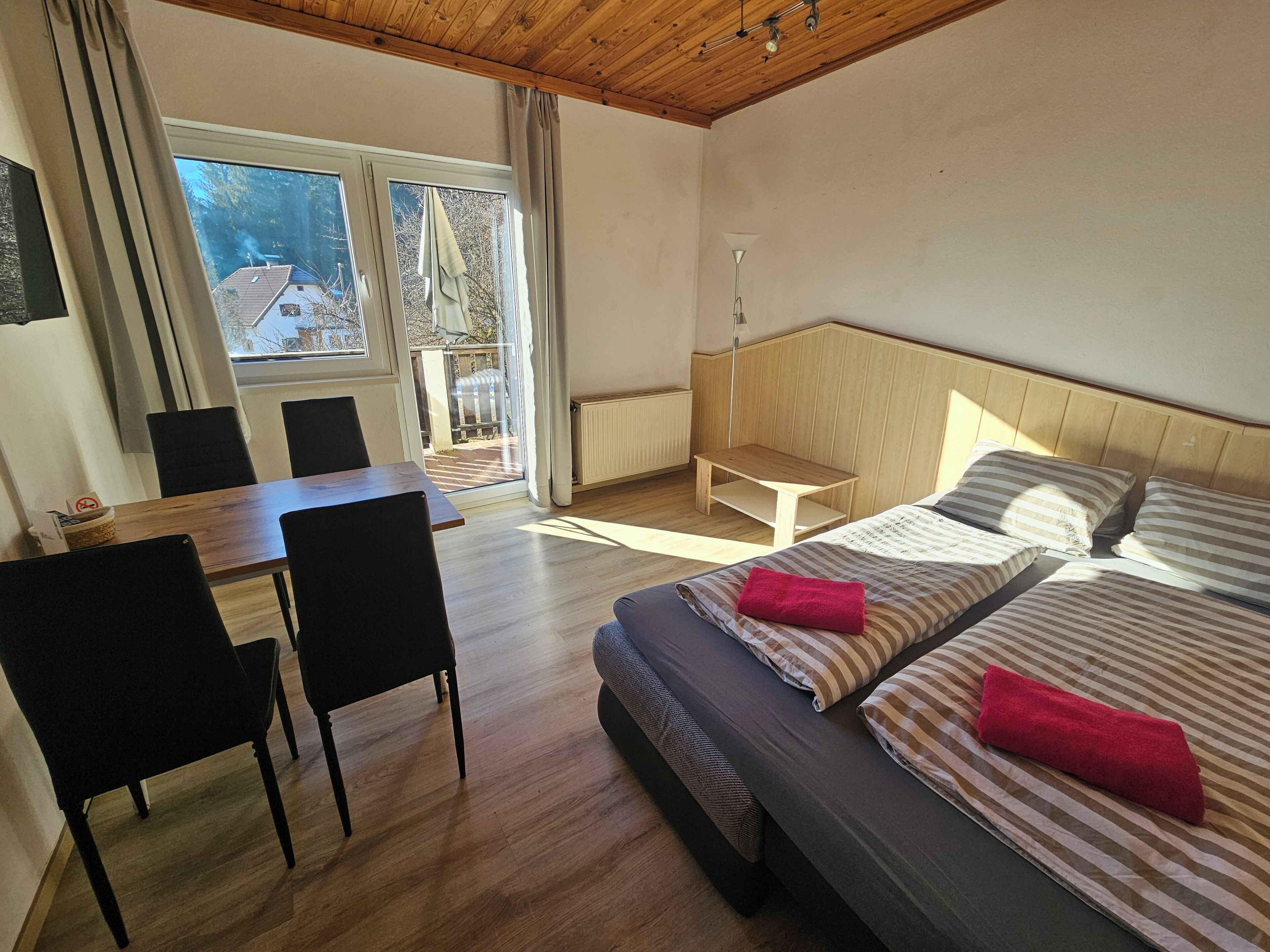 A hotel room with a bed, two chairs, a small table, and a view of the outside.