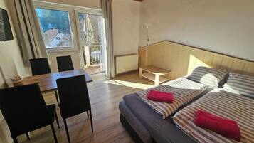 A hotel room with a bed, two chairs, a small table, and a view of the outside.