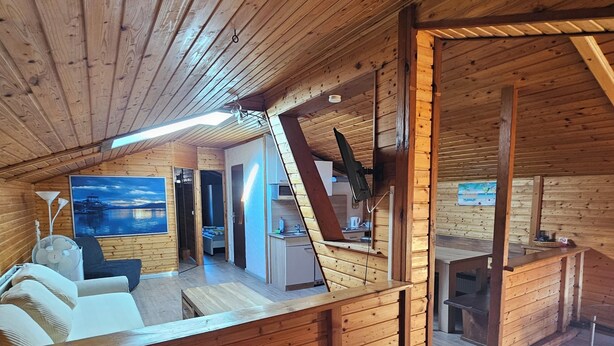 Un loft spacieux avec de hauts plafonds et des poutres apparentes, comprenant un coin salon confortable, une cuisine et un espace repas.