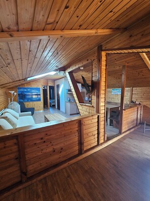 A spacious loft with a high ceiling and wooden beams, featuring a cozy seating area, a kitchen, and a dining space. - Karawanken Lodge (Finkenstein am Faaker See)