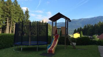 Children can play safely in this enclosed playground area with a trampoline and colorful slide surrounded by lush greenery and mountains.