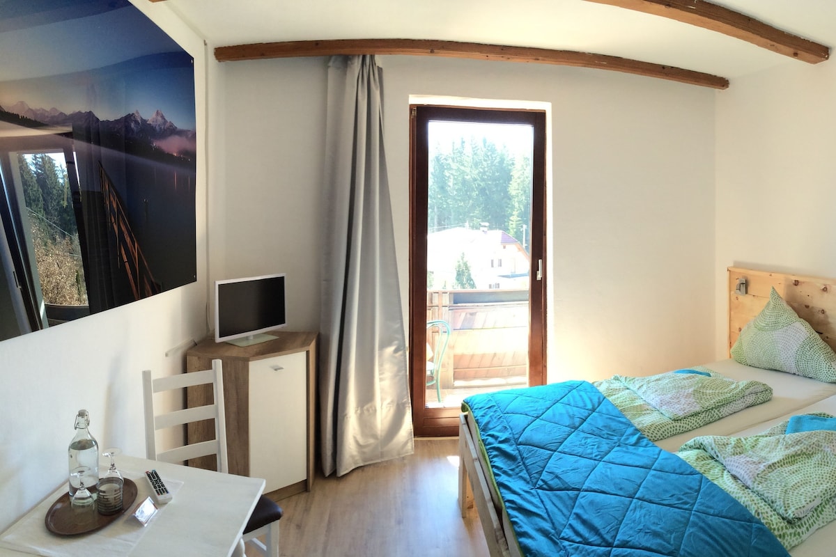 A bedroom with a bed, a desk with a computer, a window, and a view of a mountain.