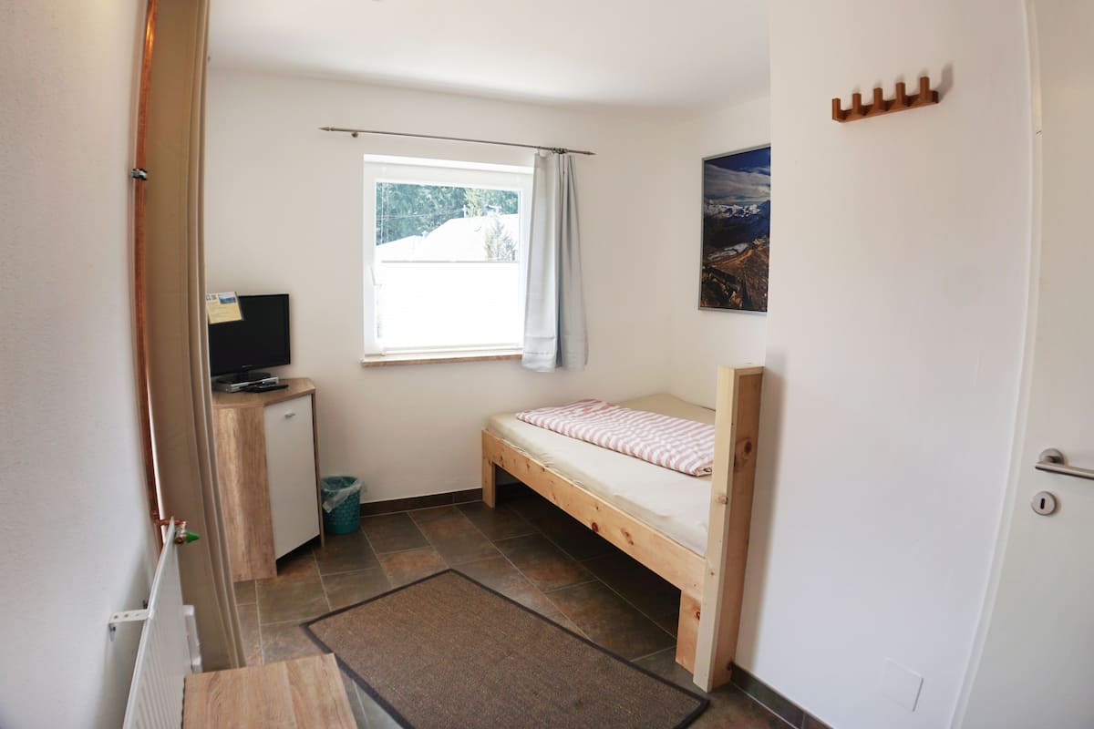 A small room with a bed, a desk with a computer, a window with curtains, and a door.