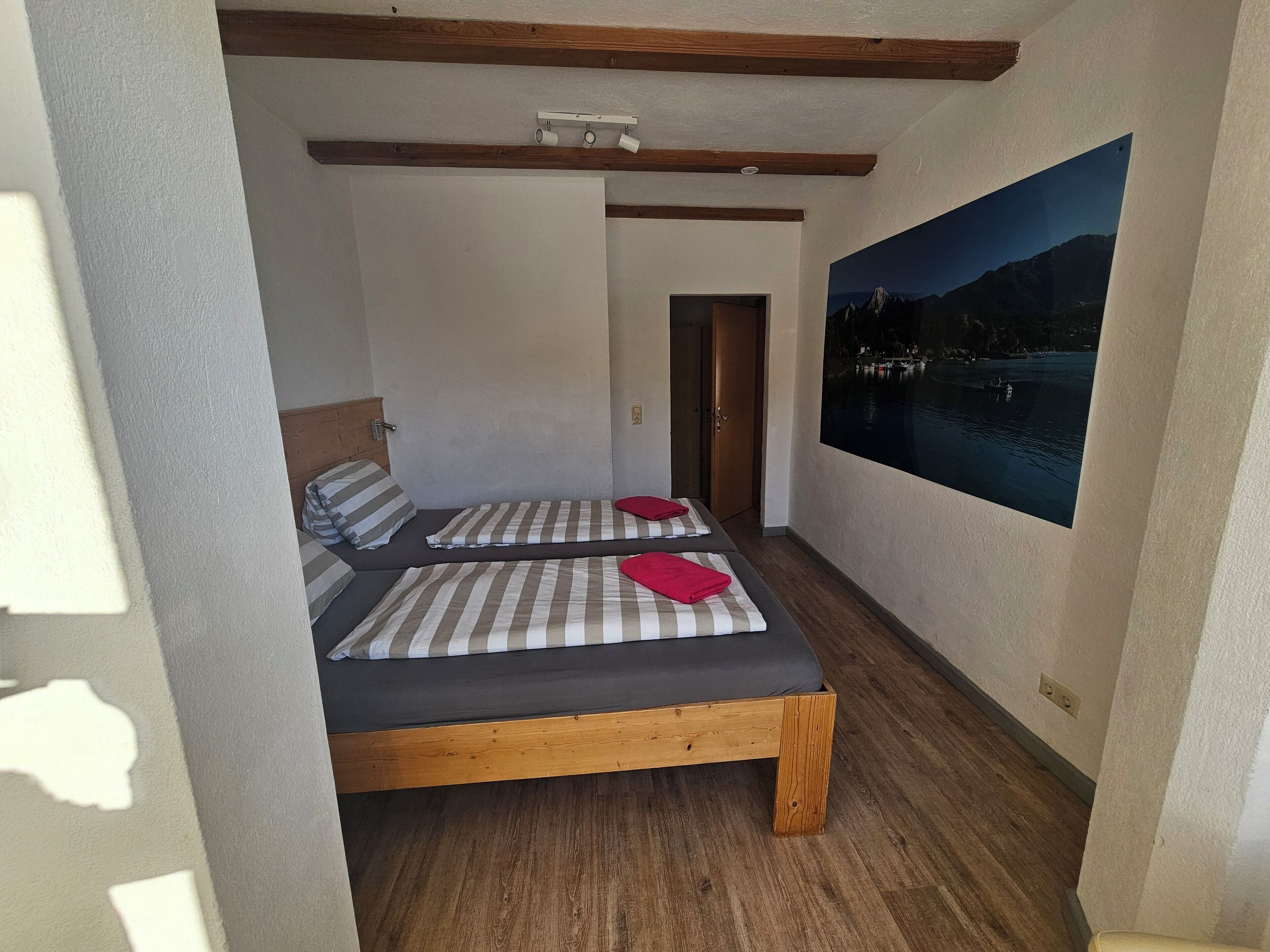 Ein Schlafzimmer mit zwei Betten, Holzbalken, einem Gemälde eines Bergsees und einer Tür zu einem anderen Raum.