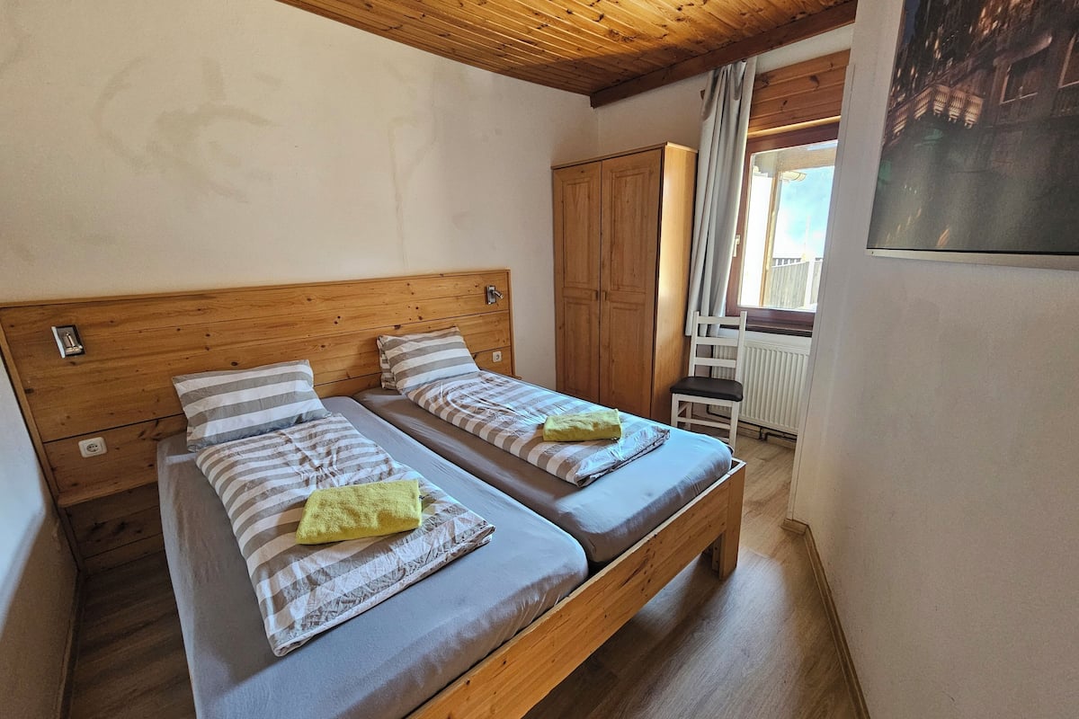 A room with two wooden beds, a wooden wardrobe, and a window with curtains.