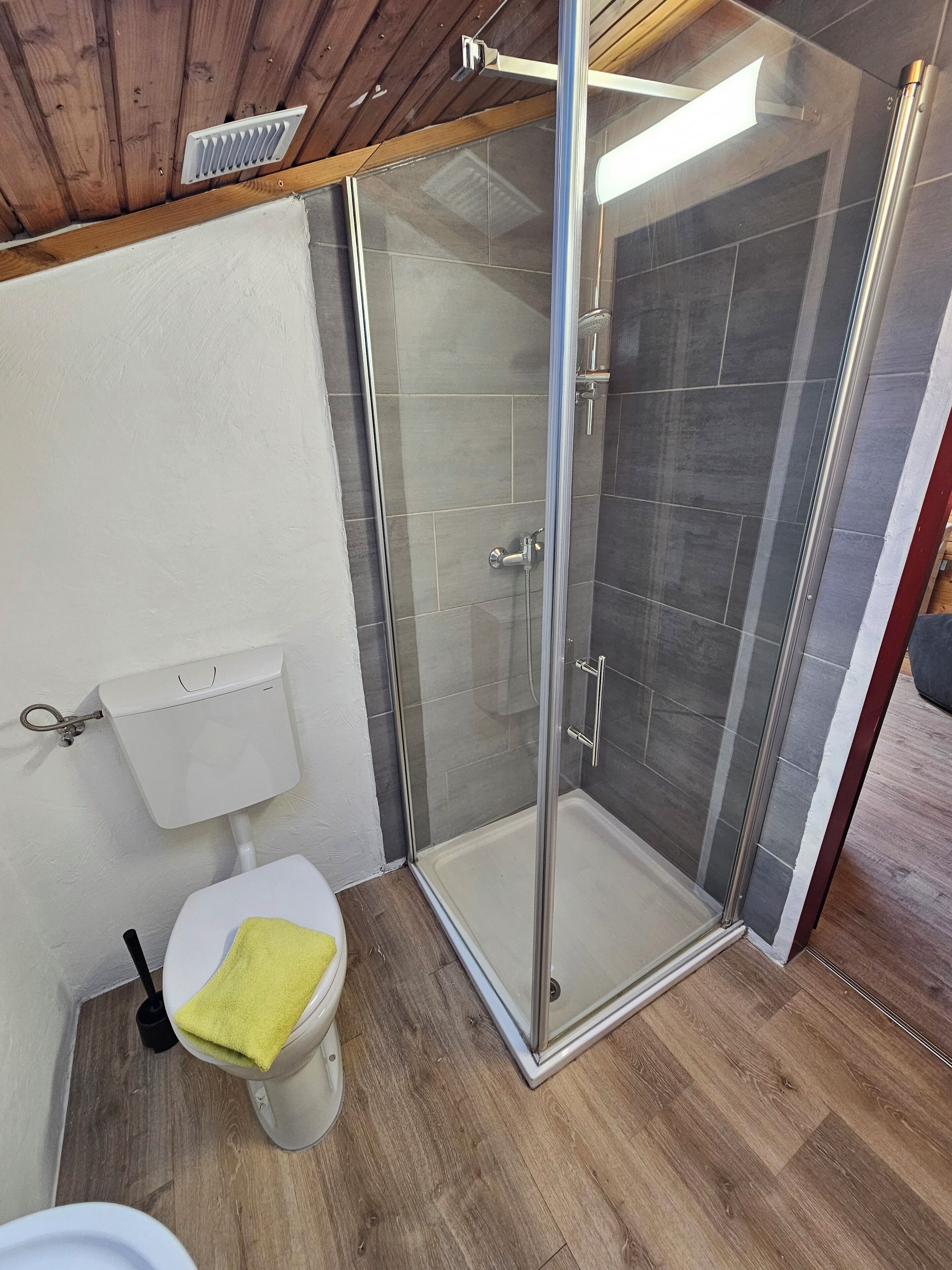 Un baño moderno con ducha de vidrio, un inodoro con una toalla amarilla y un tanque de inodoro blanco.