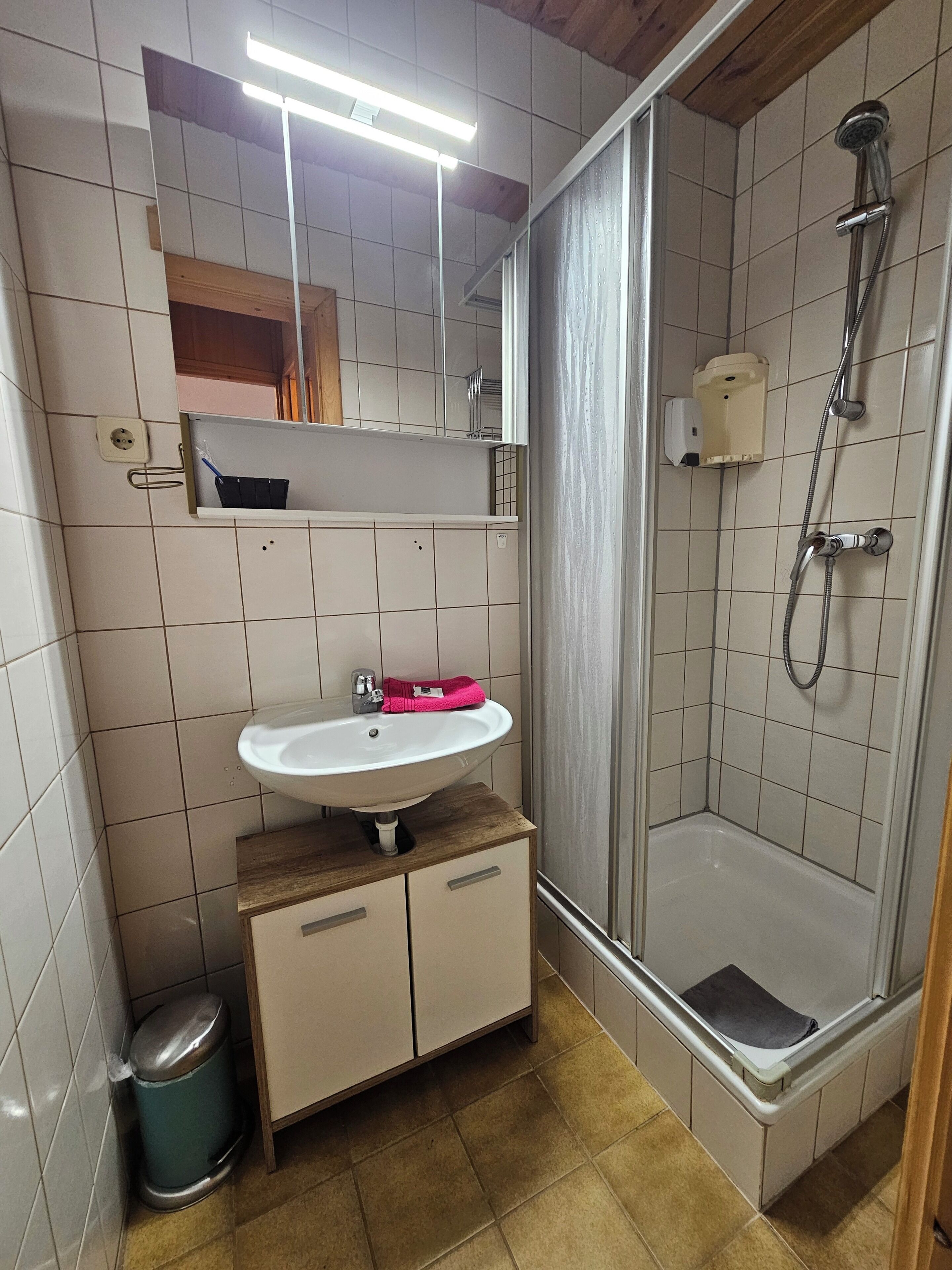 A bathroom with a sink, mirror, shower, and tiled walls.
