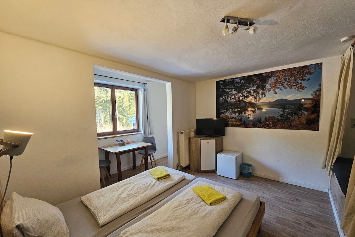 A room with two beds, a desk, a television, and a painting of a landscape.
