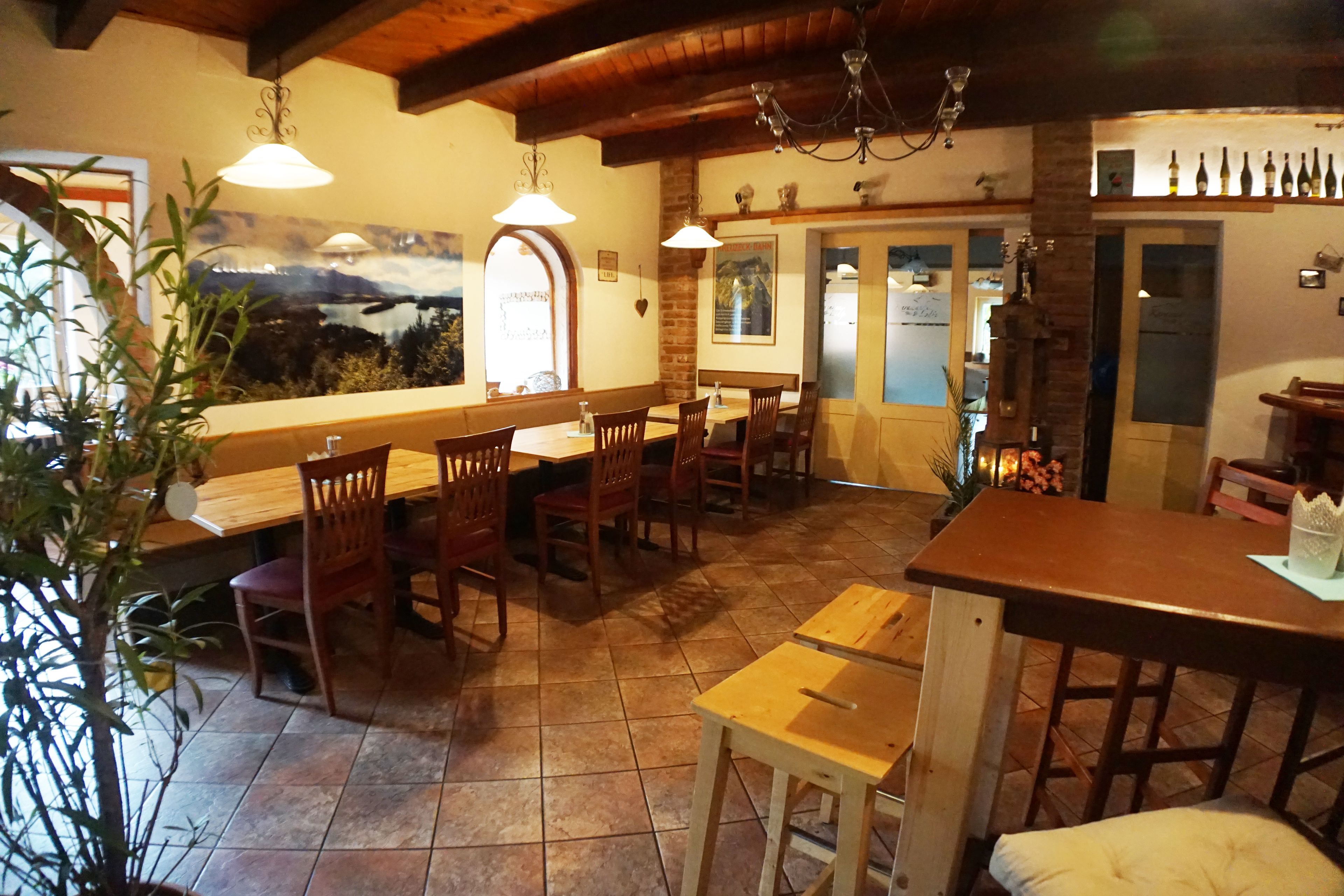 A restaurant interior with wooden tables and chairs, a bar area, and a view of the outdoors through a window.
