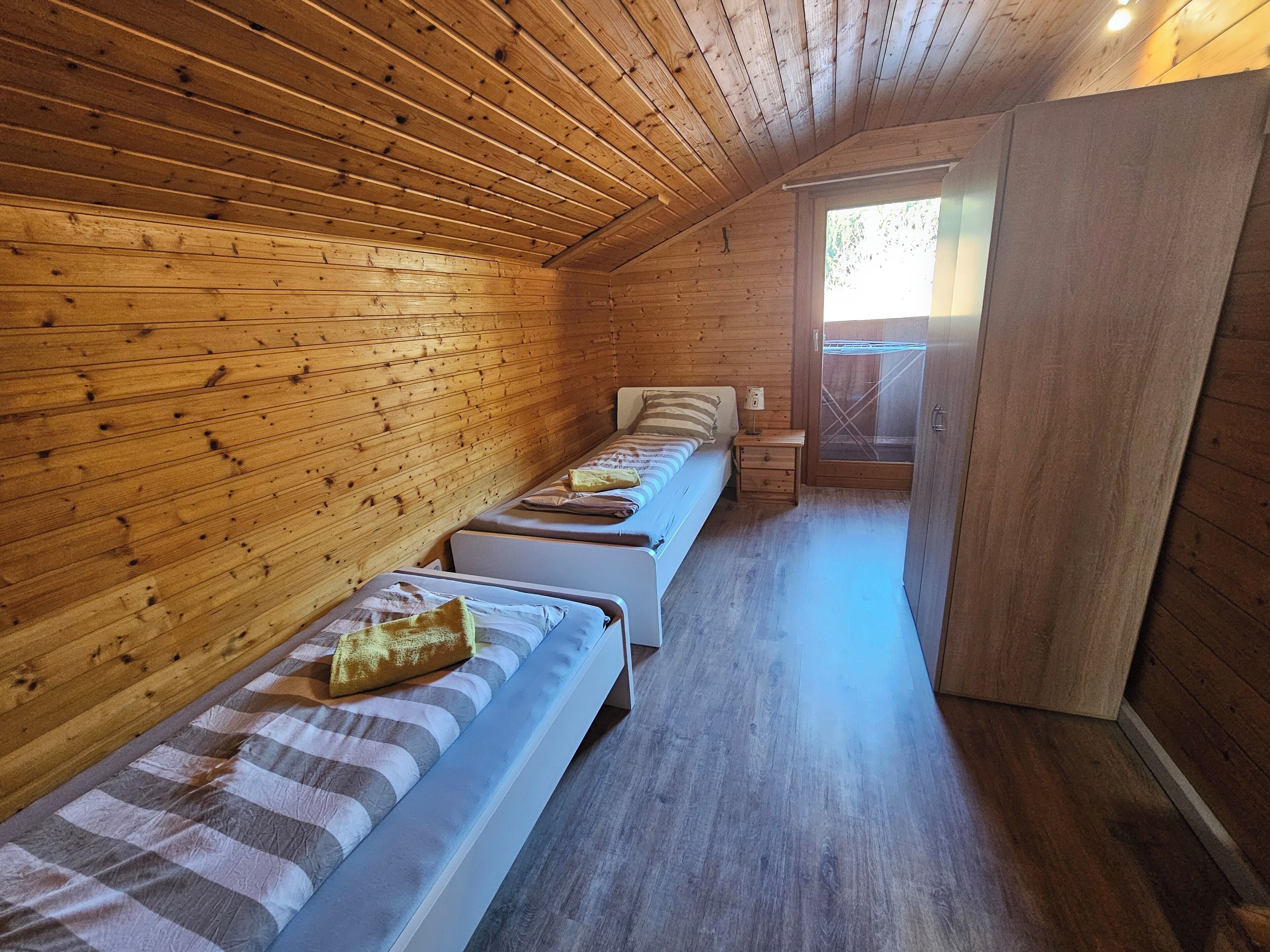 A cabin with wooden walls and floors, two single beds, a small table, and a window.