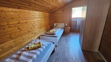 A cabin with wooden walls and floors, two single beds, a small table, and a window.