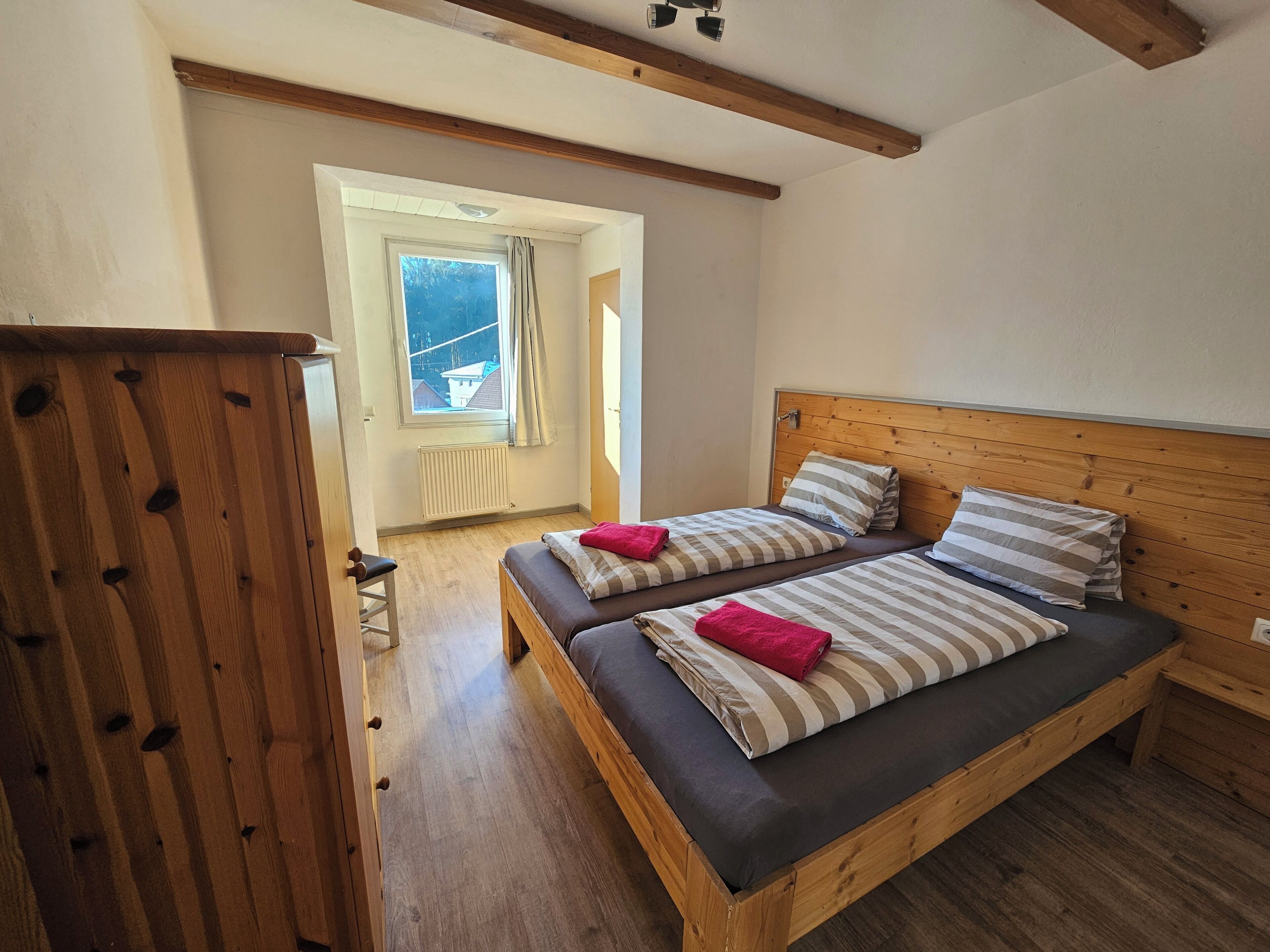 A room with two beds, wooden beams, a window with a view, and a radiator.