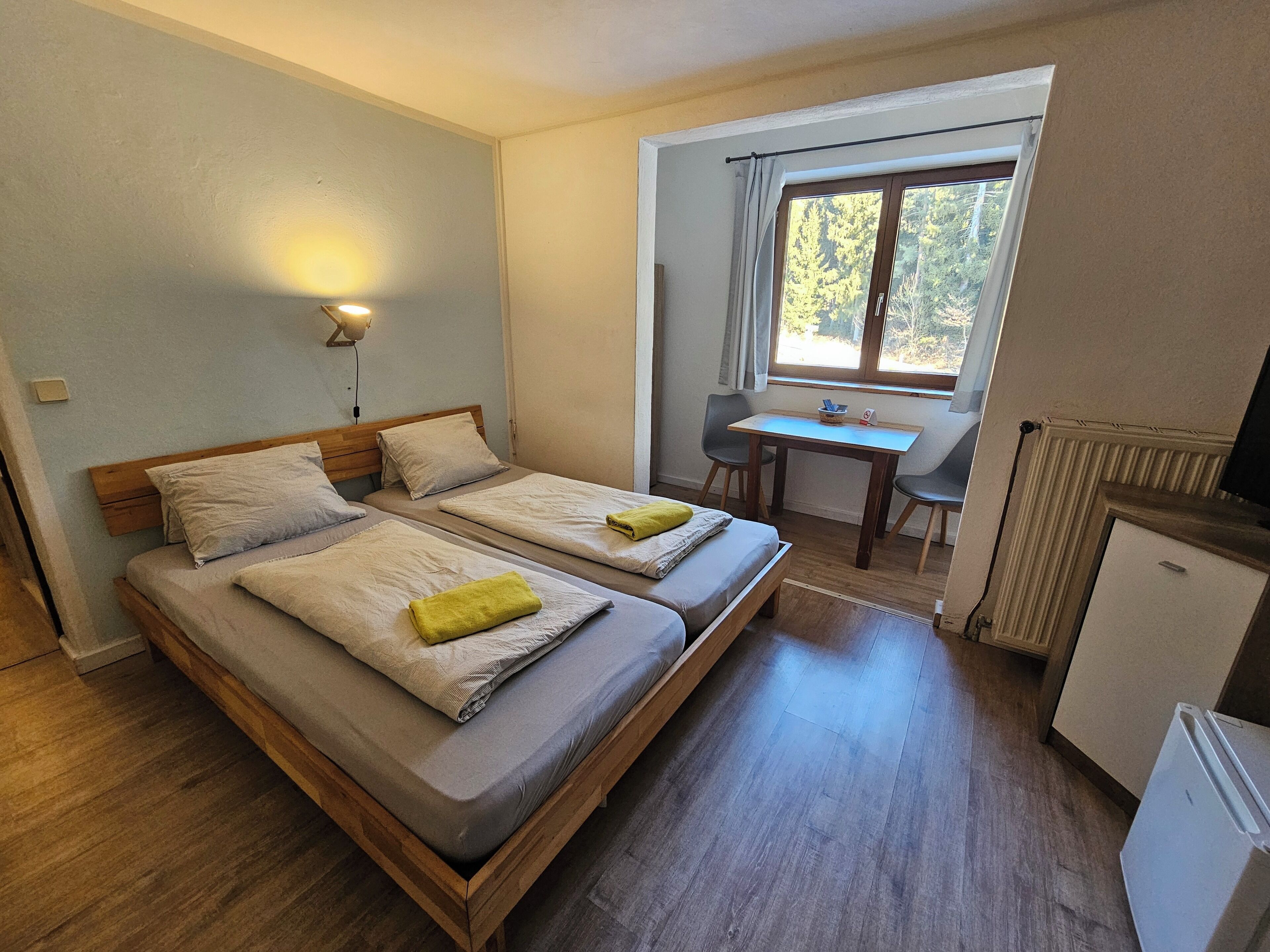 Ein Zimmer mit zwei Einzelbetten, einem kleinen Tisch, einem Stuhl, einem Schreibtisch und einem Fernseher.