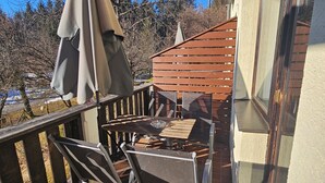 Un balcon avec une table et des chaises, une clôture en bois et une vue sur des arbres et un immeuble.
