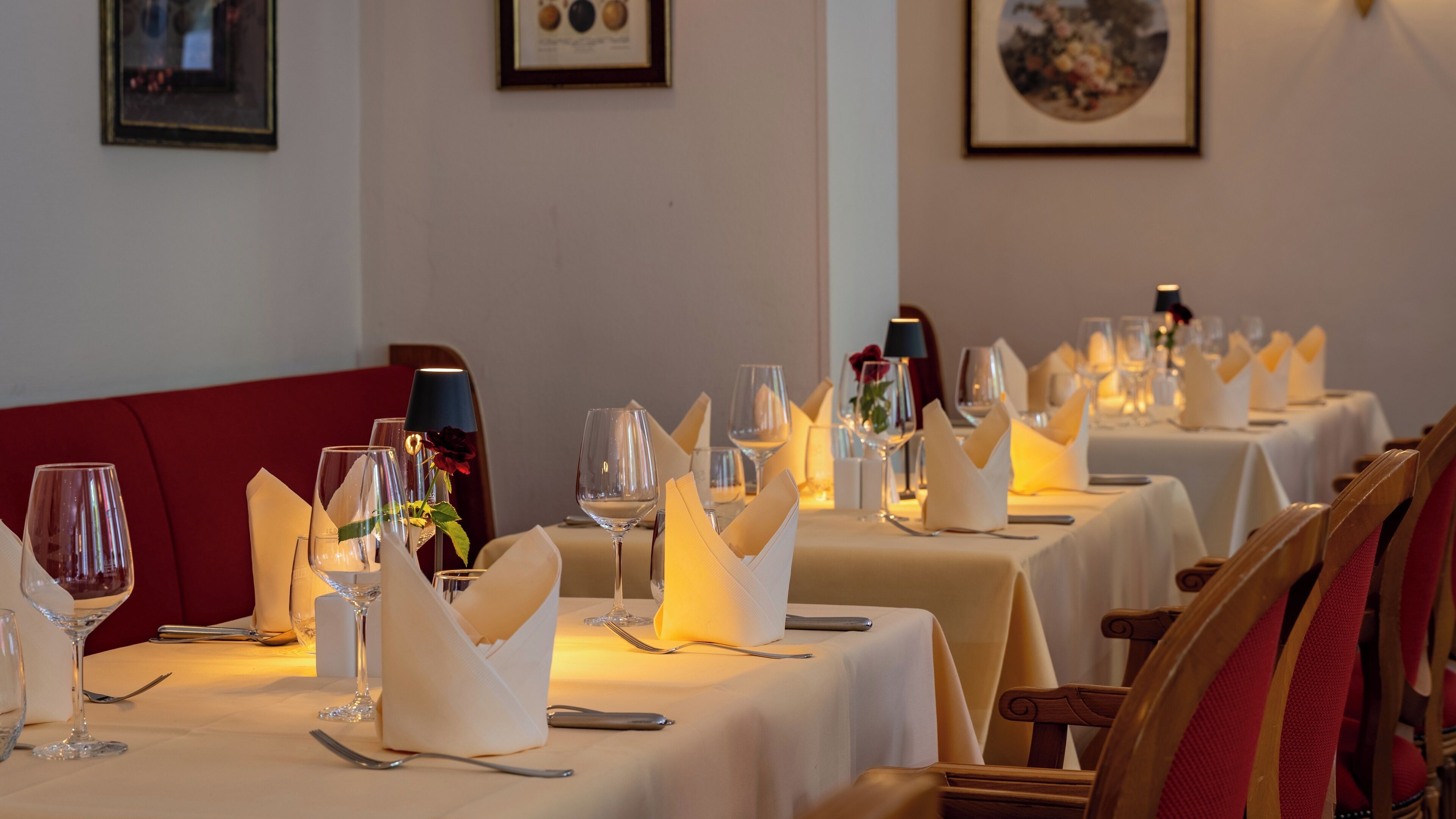 Una sala ristorante con tavoli apparecchiati, tovaglie bianche, bicchieri da vino e tovaglioli.