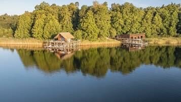 Una cabaña junto al lago con muelle y un bote, rodeada de un bosque frondoso.
