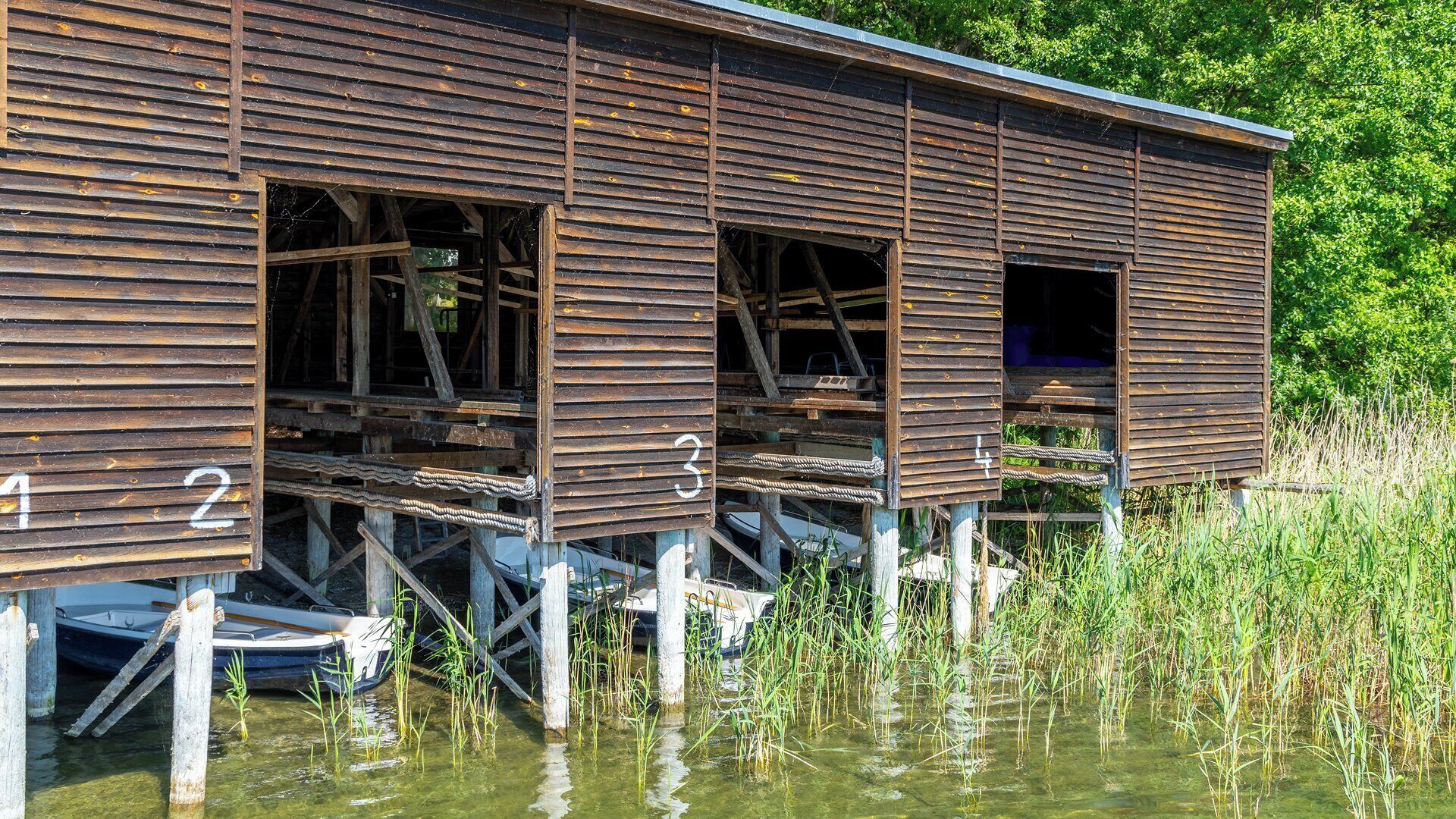 A wooden structure with numbered windows, elevated on stilts in a water body, surrounded by vegetation.