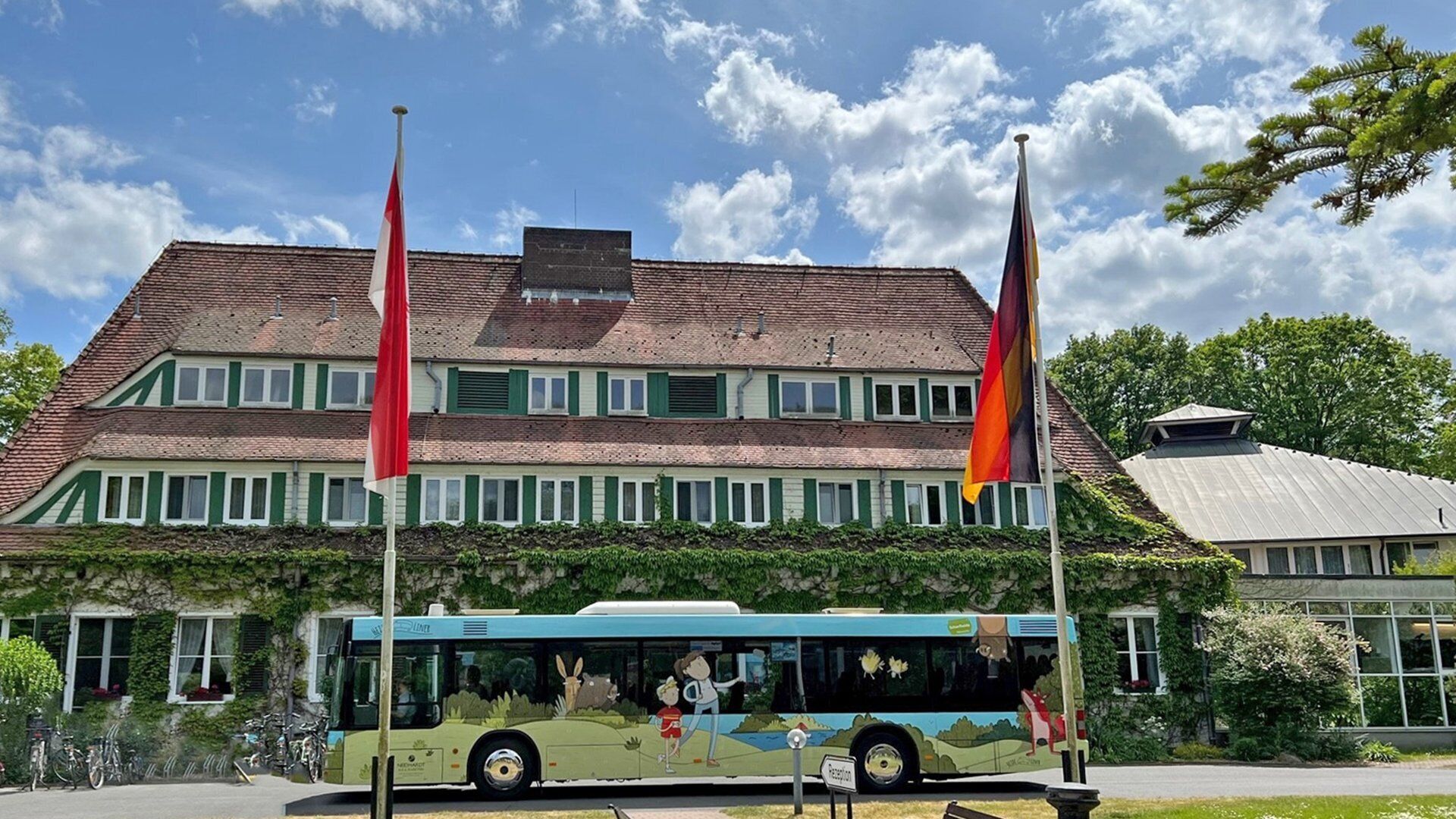 A bus with a green and white color scheme parked in front of a building with a red and yellow flag.