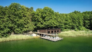 Un muelle de madera se adentra en un lago, con una cabaña y sillones de descanso.