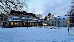A snow-covered courtyard with buildings featuring traditional architecture, including a prominent multi-story structure with a sloped roof.