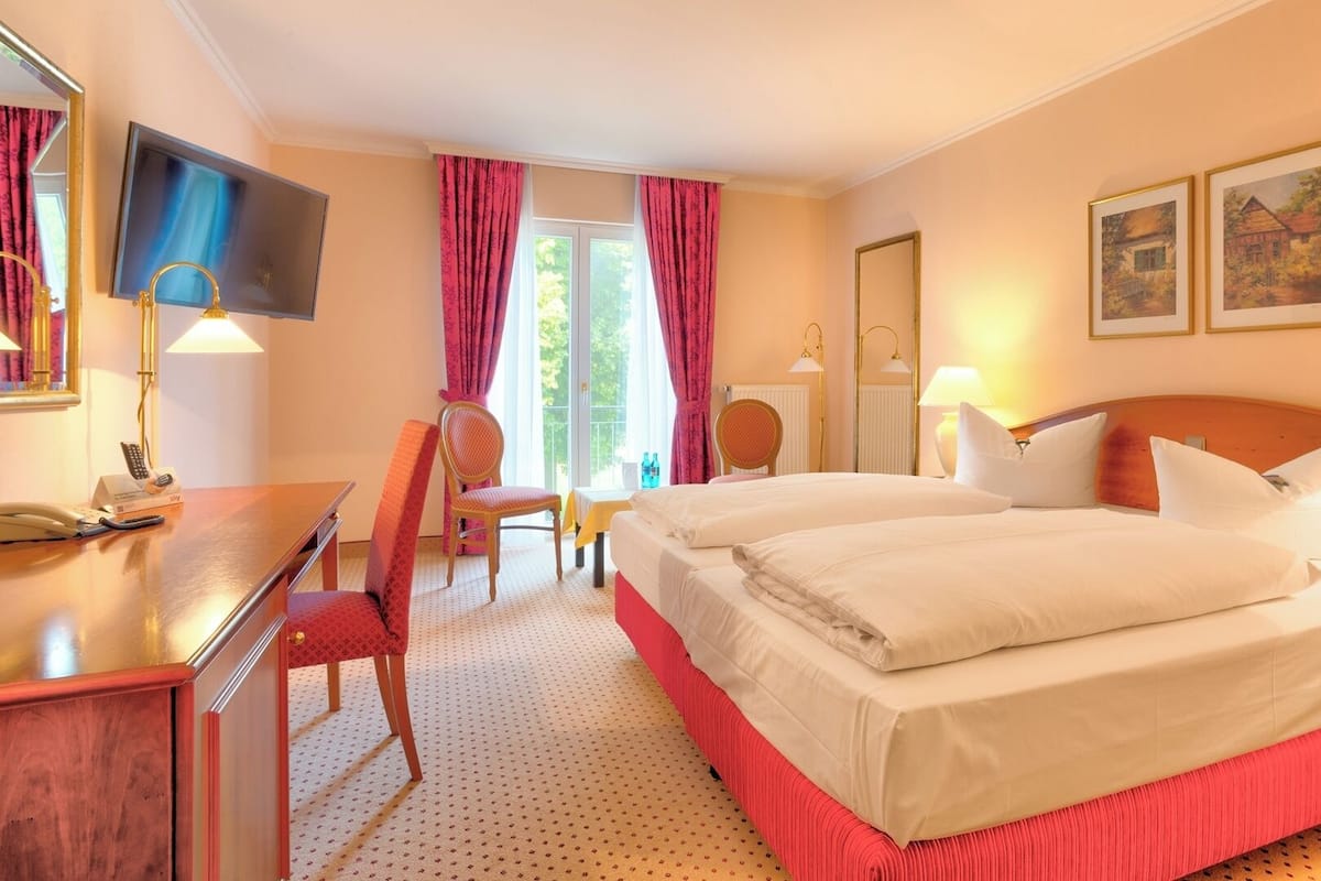 A hotel room with a bed, a desk with a telephone, a chair, a television, and two paintings on the wall.