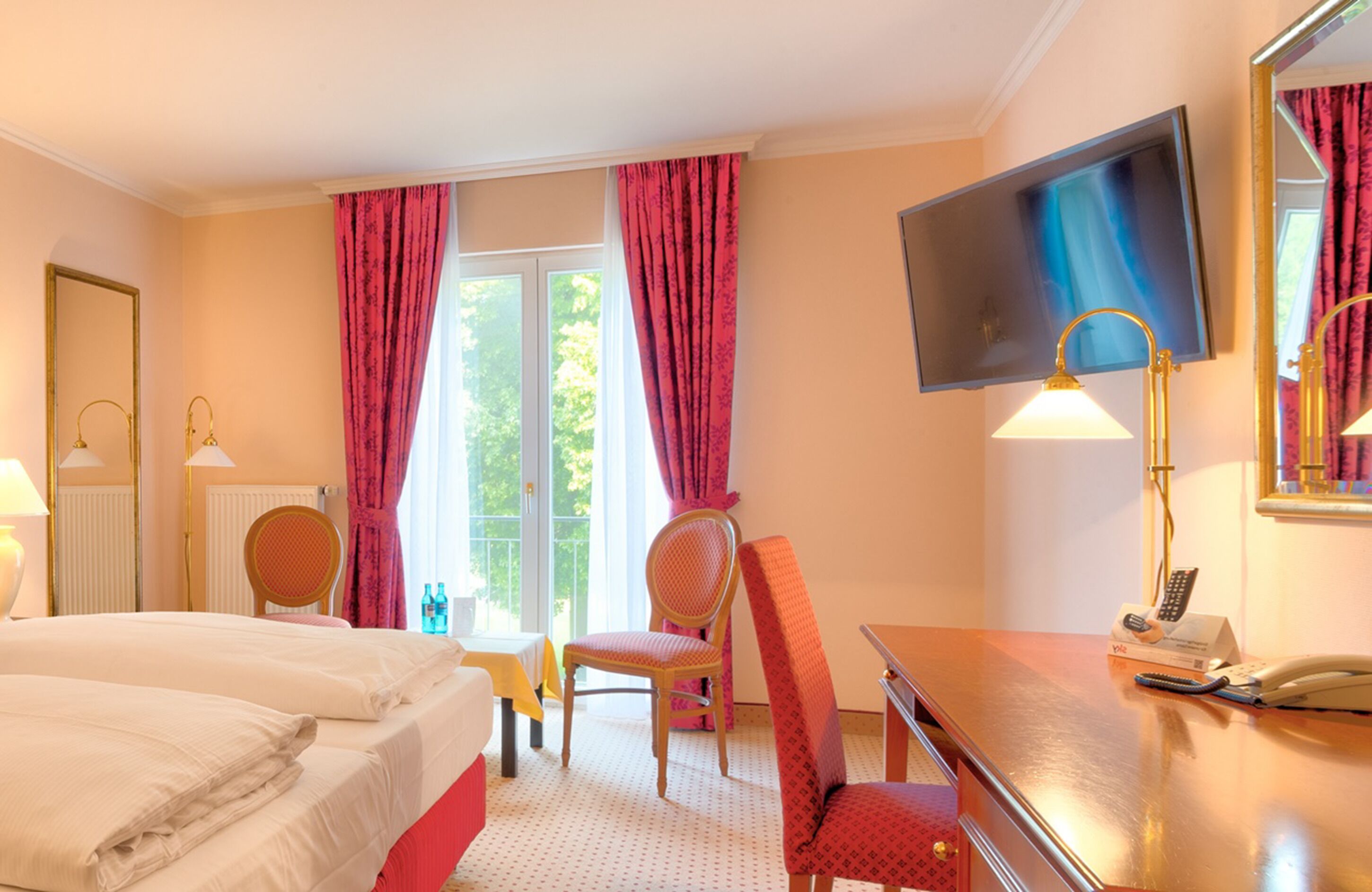 Hotelkamer met twee bedden, een bureau met telefoon en afstandsbediening, een stoel, een aan de muur bevestigde televisie en een raam met gordijnen.