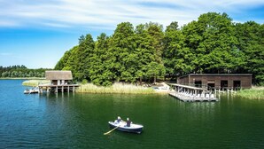 Una cabaña junto al lago con un muelle, un bote pequeño y un área boscosa.