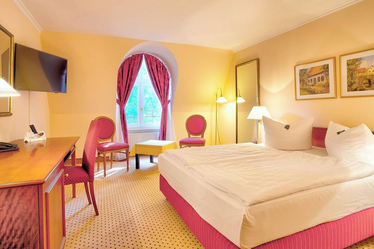 A hotel room with a bed, desk, chairs, and a TV.