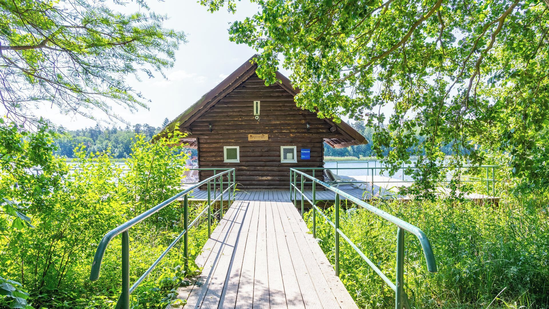 Une cabane en bois avec une terrasse en bois qui y mène, le tout entouré d’une végétation luxuriante.