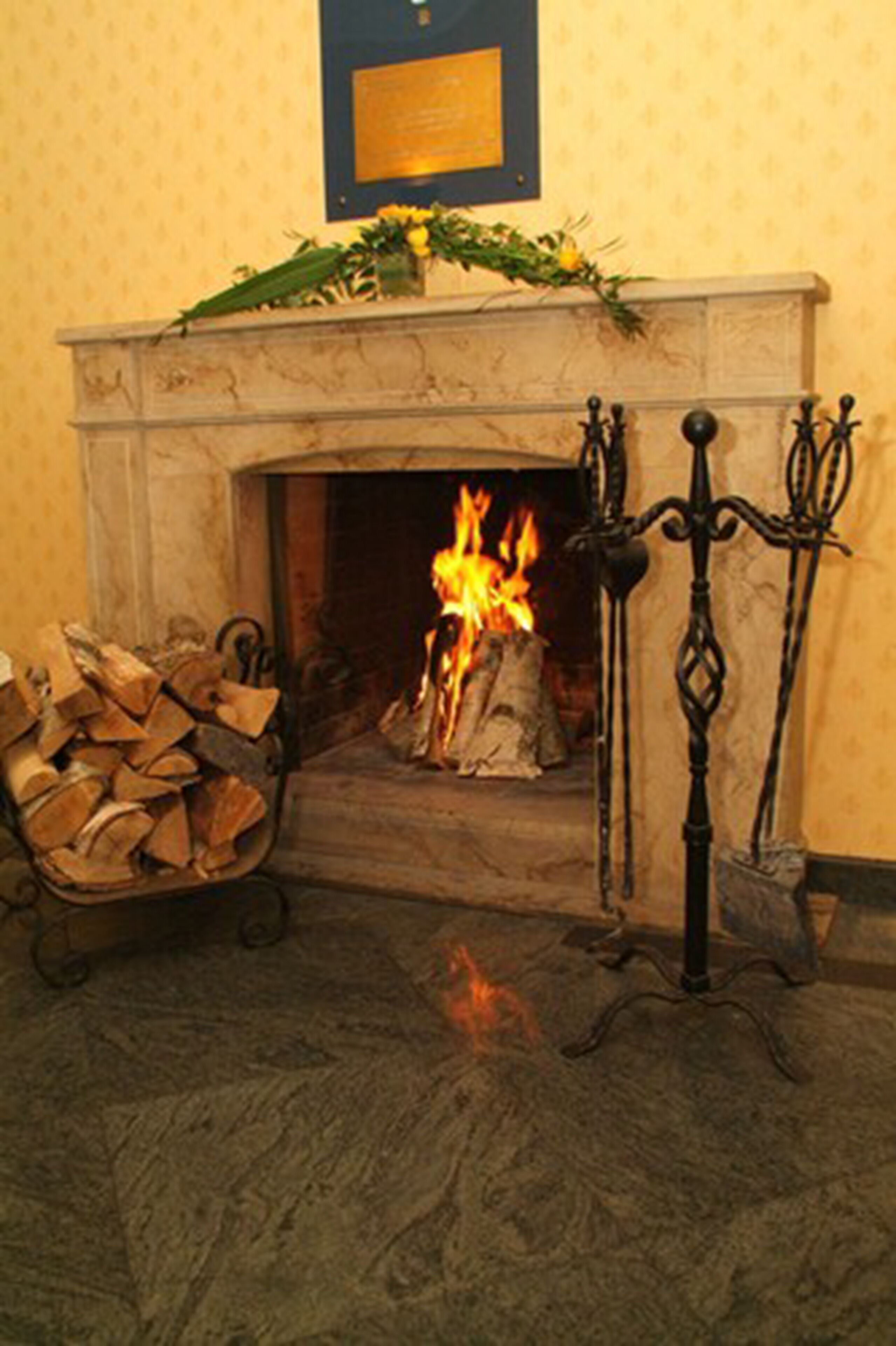 A fireplace with a burning fire, a pile of firewood, and a decorative wreath on the mantel.