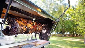 A rotisserie with a large, rotating spit of meat, a metal grill, and a window.