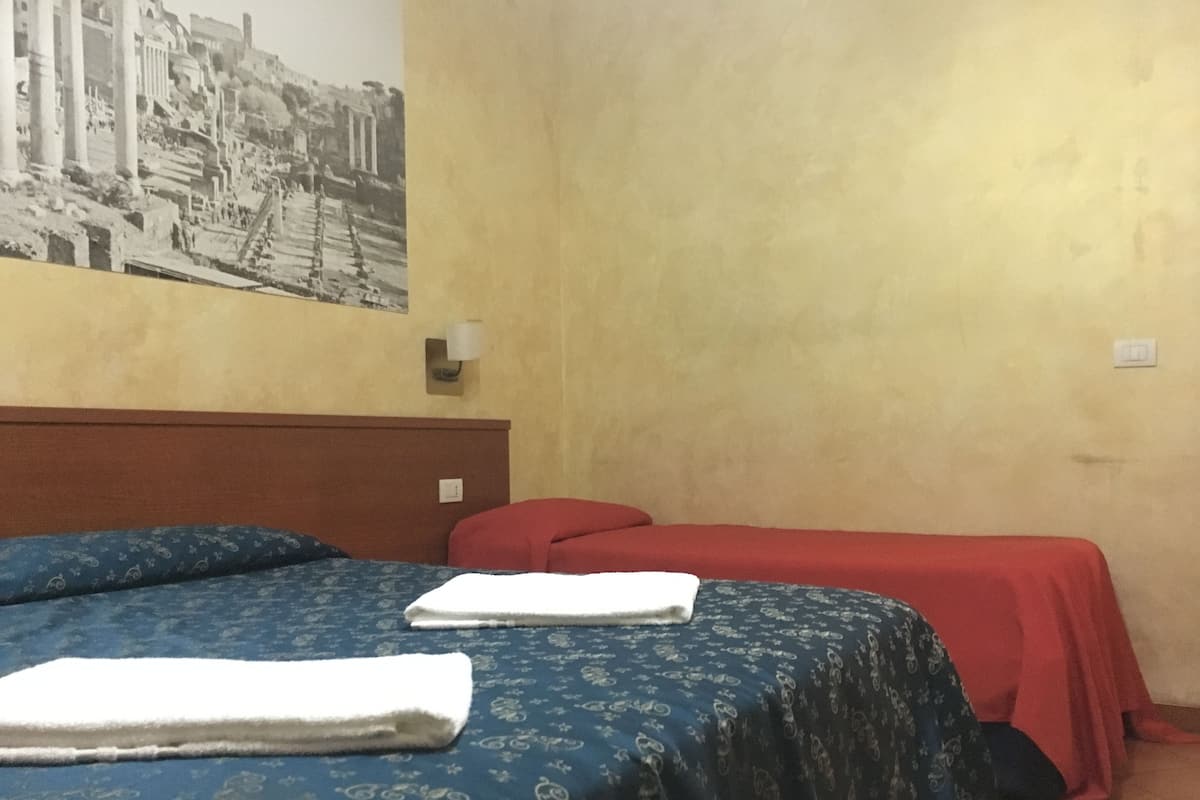 A hotel room with a bed, a red sofa, and a wall-mounted lamp.