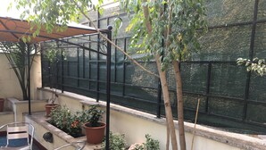 A balcony with potted plants, a metal chair, and a window with a mesh screen. - Best Location in Rome (Rome)