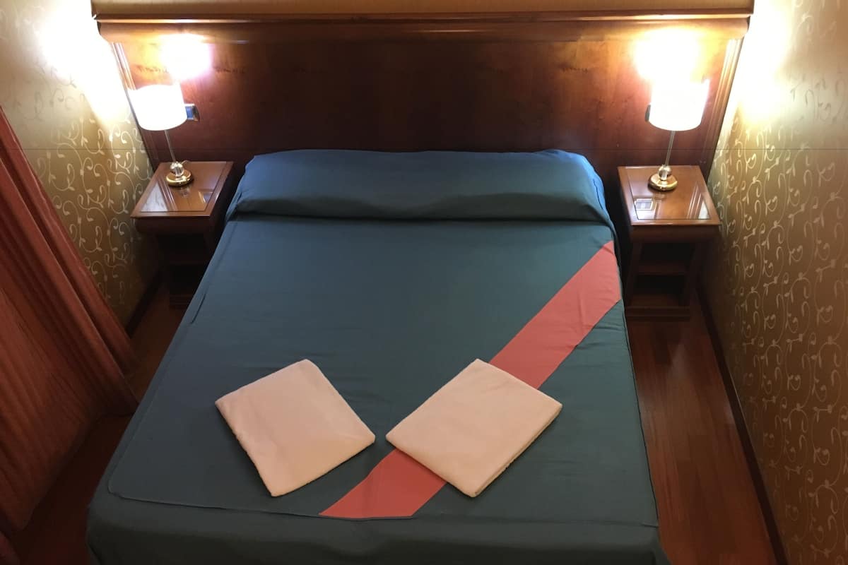 A neatly made bed with a teal bedspread and two folded towels, flanked by two bedside lamps on wooden nightstands.