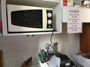 Una cocina con microondas blanco, máquina de café y un cartel que indica los precios del agua fría y Coca-Cola.