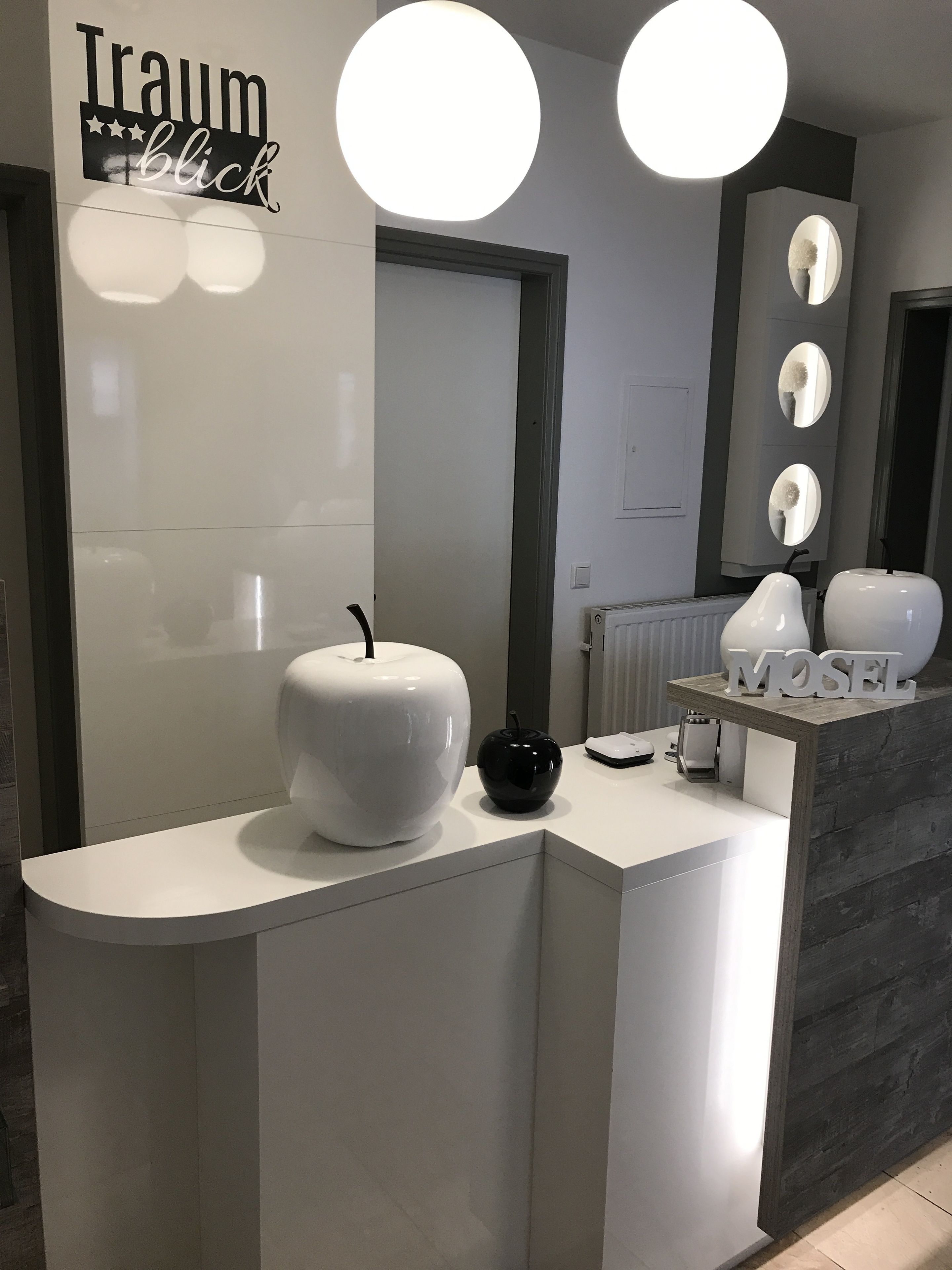 A modern reception desk with a white countertop, two large round lights, a black decorative bowl, and a sign that reads "Traumblick".