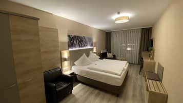 A modern hotel room with a large bed, a desk, a chair, and a small table.