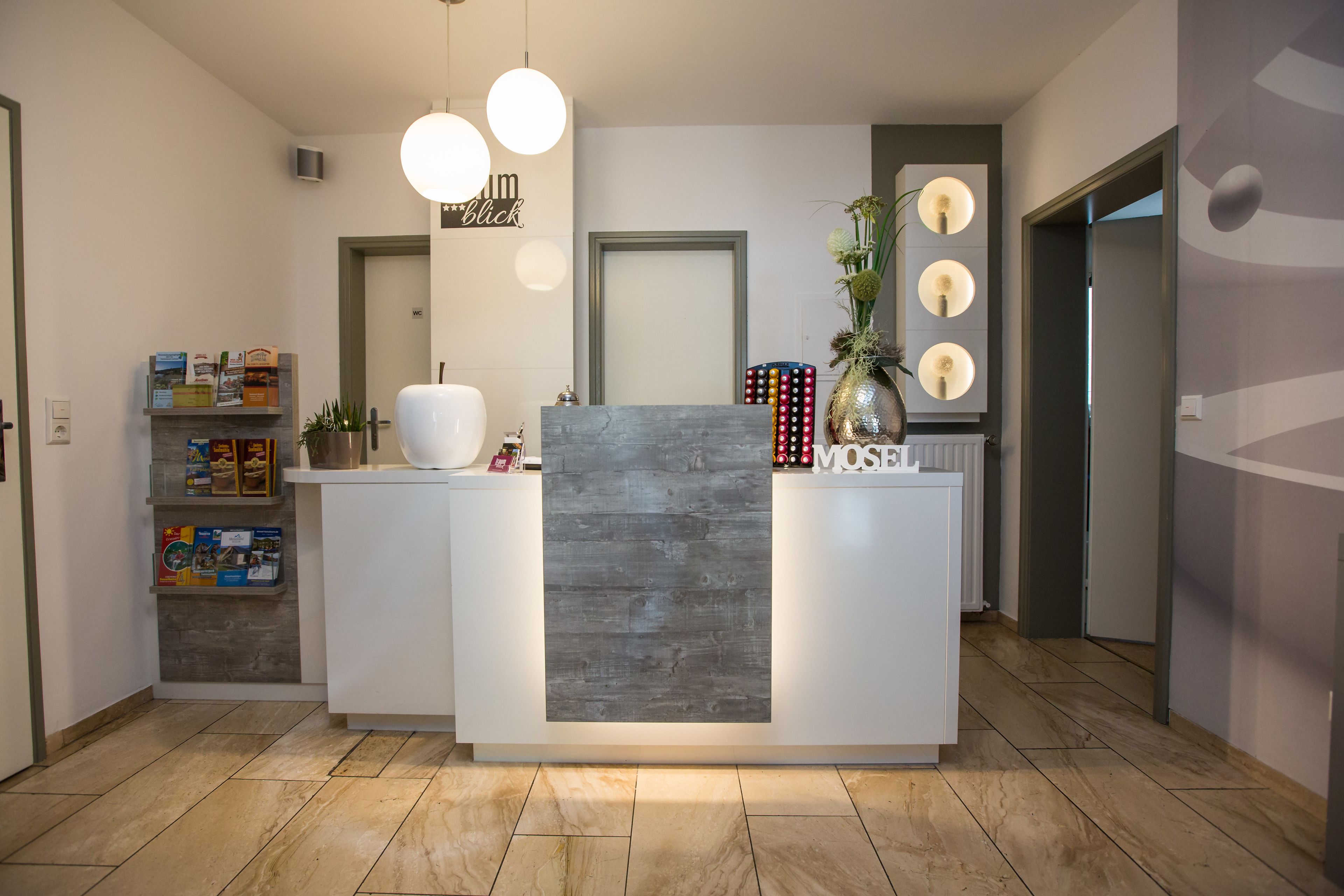 A reception area with a modern design, featuring a central desk, a mirror, and a wall-mounted light fixture.