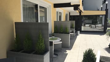 A patio area with wicker furniture, potted plants, and a view of the street.