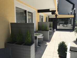A patio area with wicker furniture, potted plants, and a view of the street. - Hotel Traumblick (Cochem)