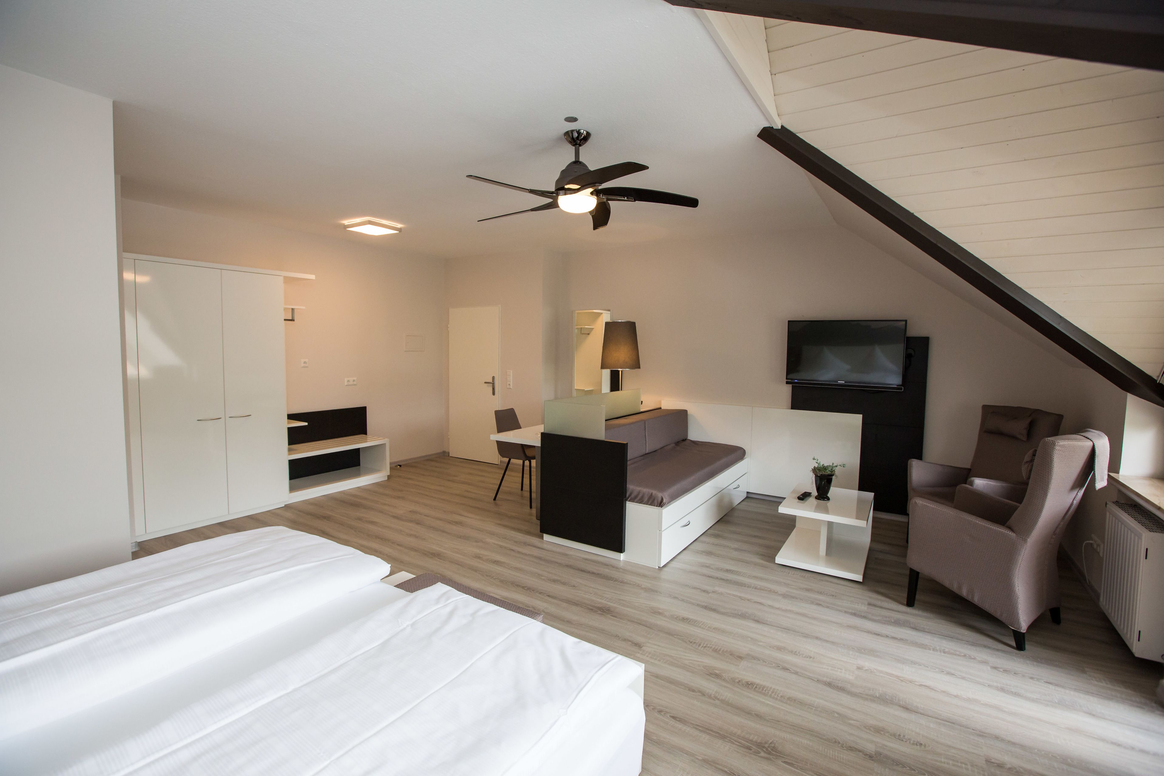 Un dormitorio moderno con cama, escritorio, silla, sofá y televisor.