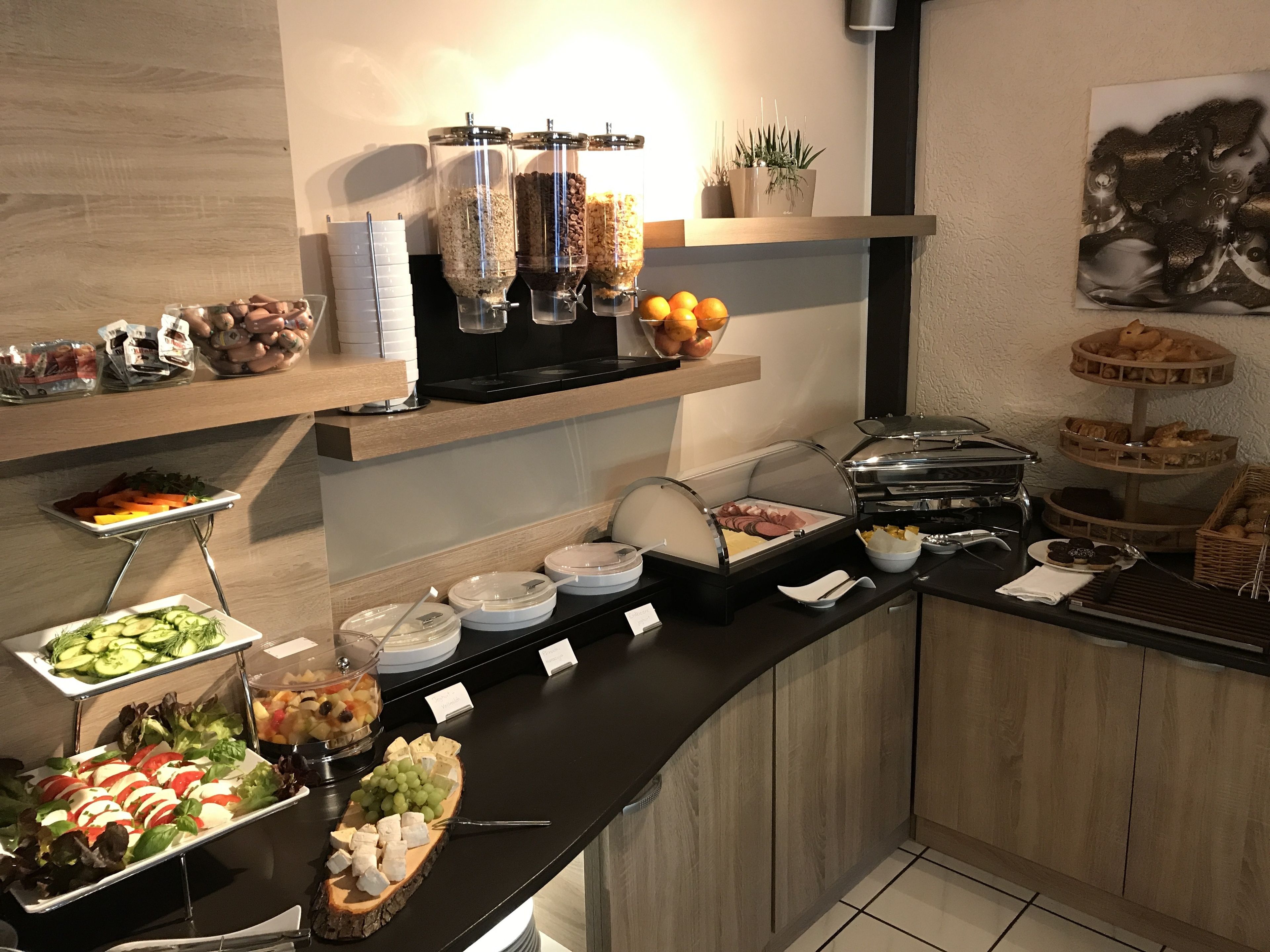 A buffet setup with various food items, including fruits, cheeses, and pastries, arranged on a counter with a modern design.