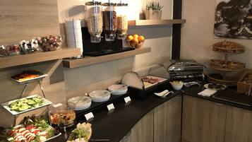 Montaje de bufé con diversas opciones de comida, como frutas, quesos y pasteles, dispuestas sobre un mostrador de diseño moderno.