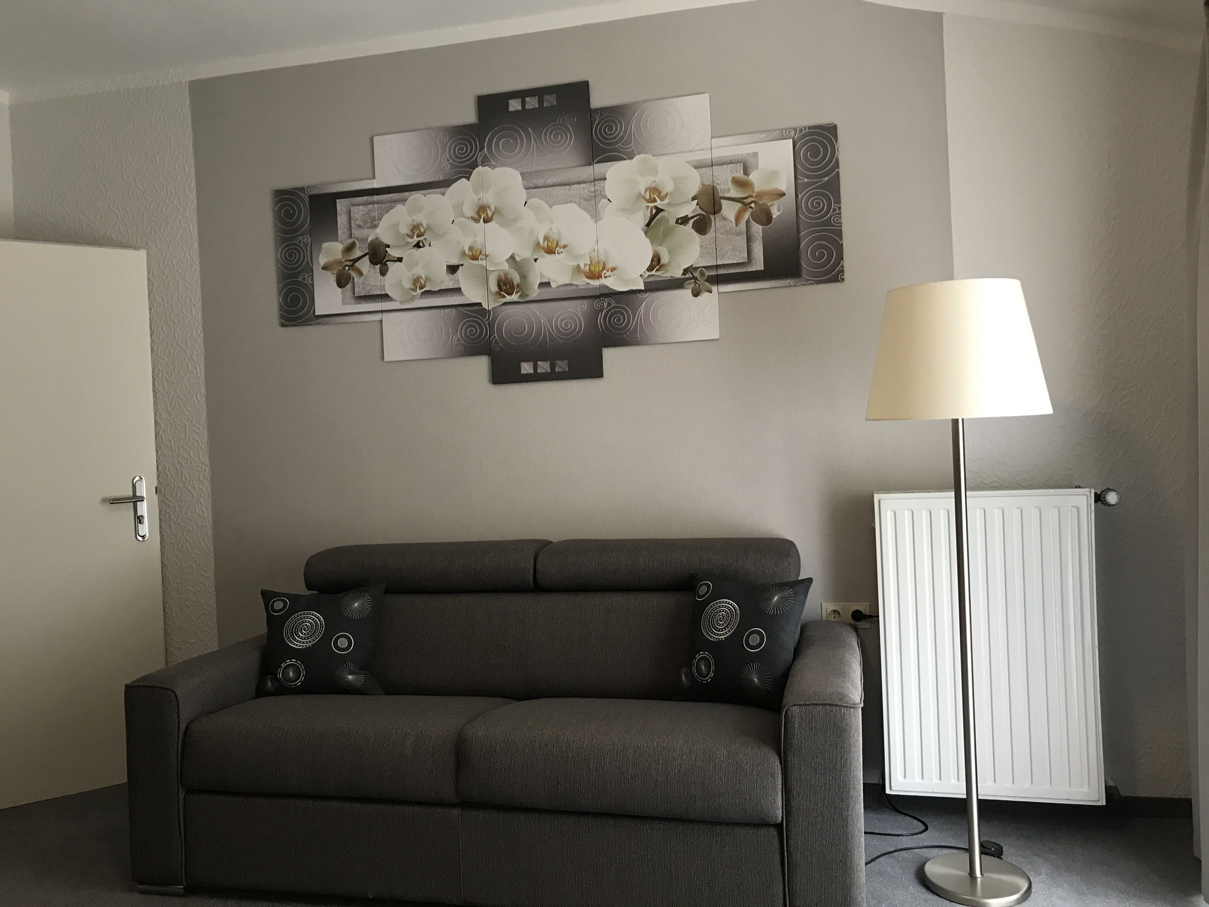 A modern living room with a grey sofa, decorative wall art, a floor lamp, and a radiator.