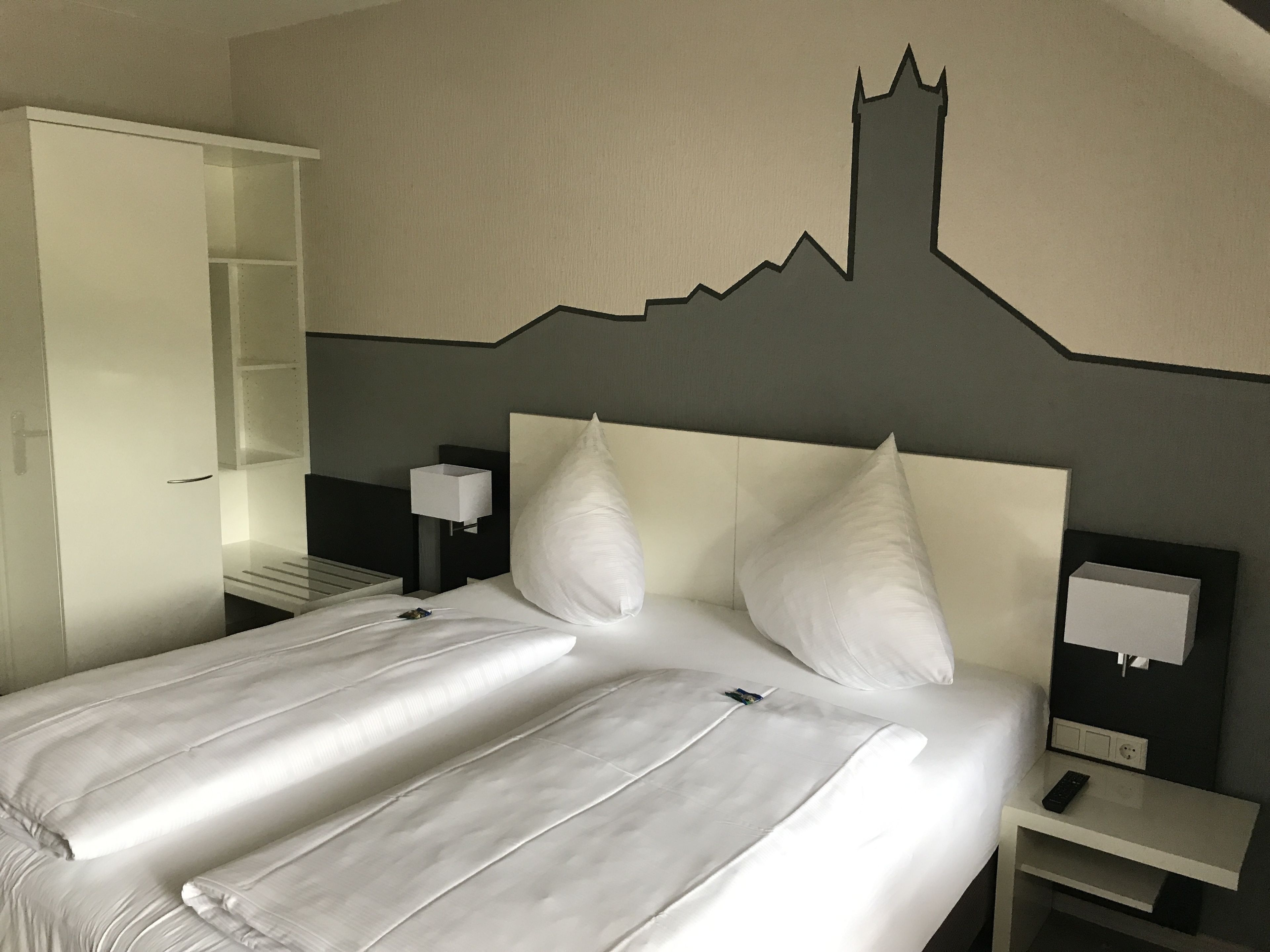Une chambre d’hôtel comprenant un lit, une table de chevet, un téléviseur fixé au mur et une armoire.