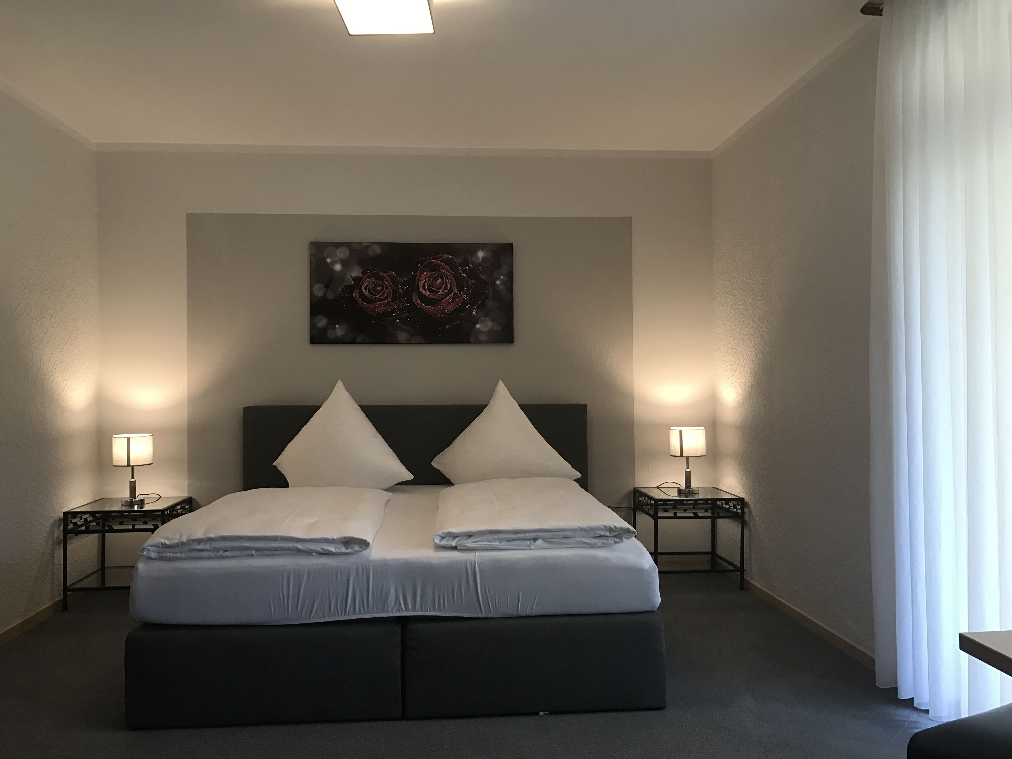 Una habitación de hotel con una cama grande, dos mesitas de noche, un cuadro en la pared y una ventana con cortinas.