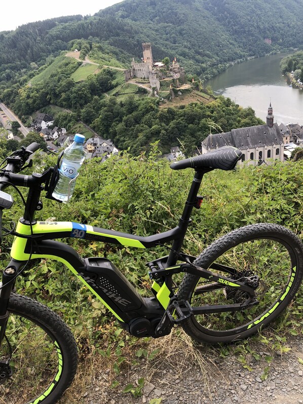 A mountain bike parked on a rocky path with a scenic view of a castle and river in the background. - Hotel Traumblick (Cochem)