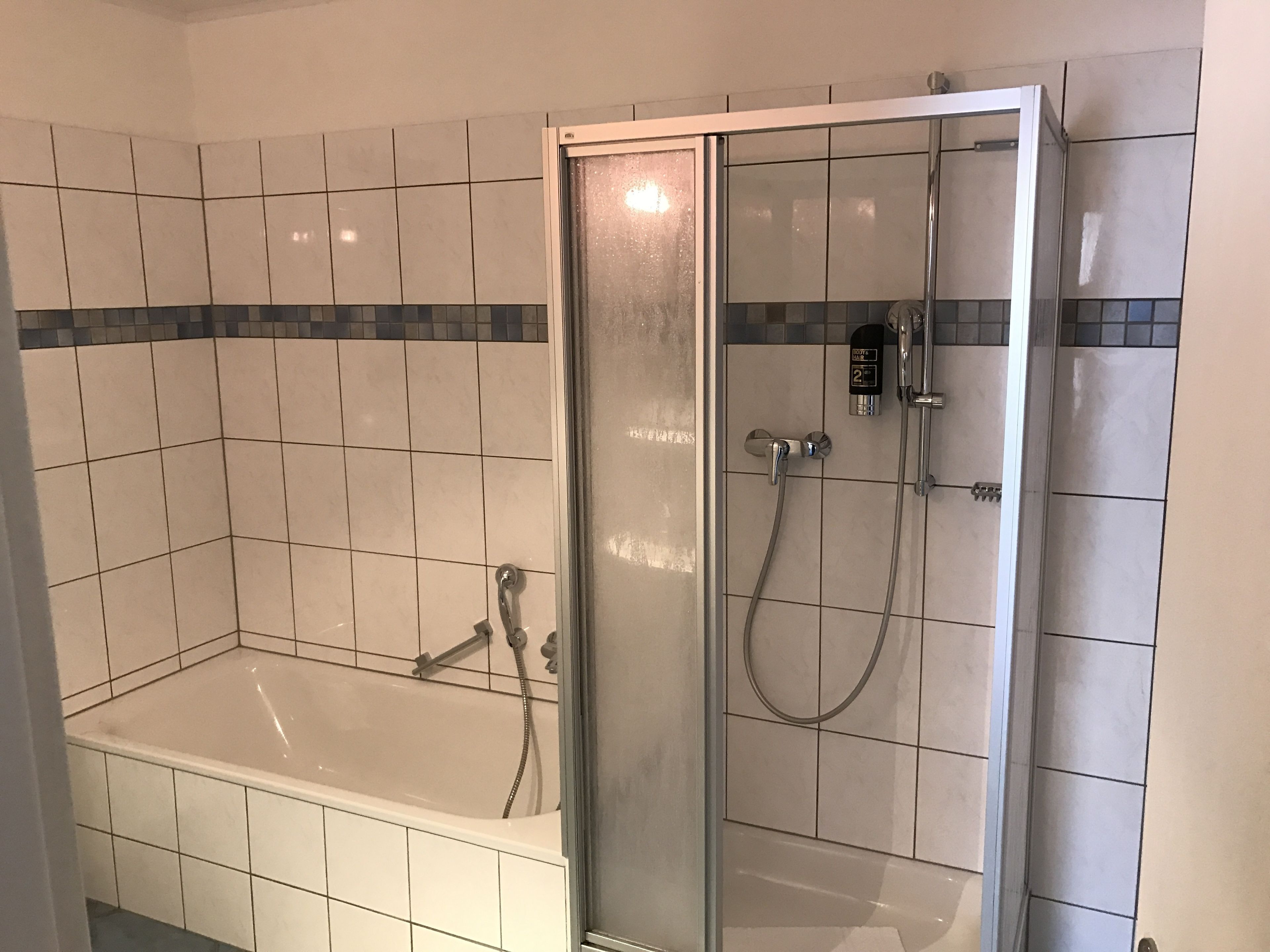 Une salle de bain avec une baignoire, une douche à parois de verre et des murs carrelés.